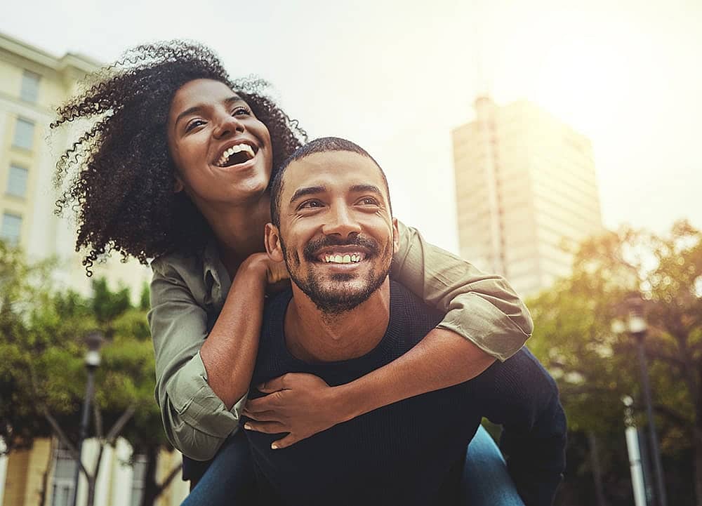 Man carrying woman on his back smiling in city